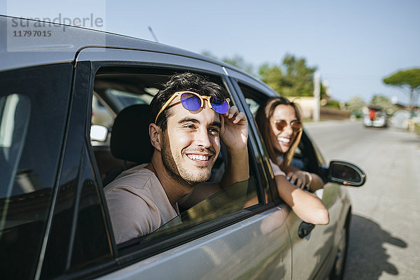 Glücklicher junger Mann und Frau in einem Auto mit Blick aus dem Fenster
