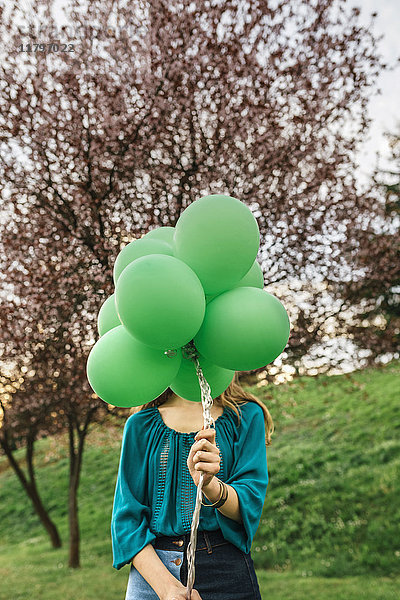 Junge Frau versteckt sich hinter grünen Luftballons