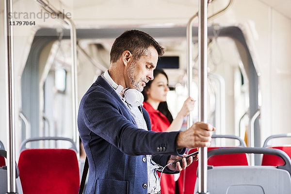 Geschäftsmann mit Smartphone und Kopfhörer auf Busfahrt