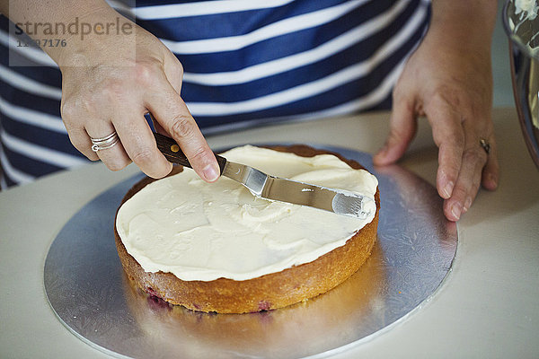 Nahaufnahme aus hoher Perspektive einer Person  die eine blau-weiß gestreifte Schürze trägt  auf der Sahne über einen Kuchen gestreut wird.