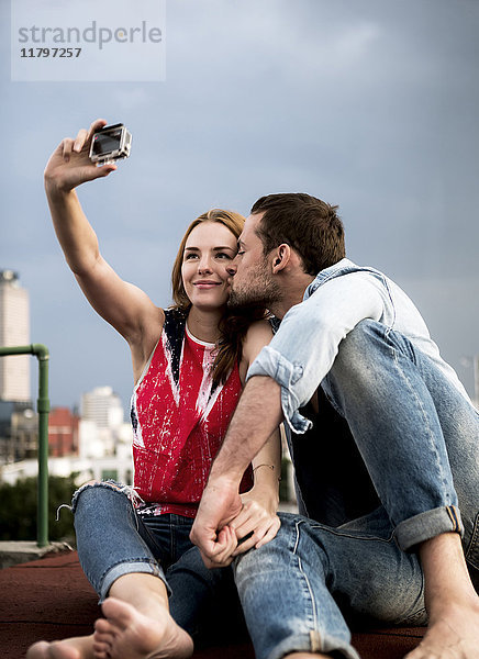 Ein Pärchen posiert für einen Selfie auf dem Dach einer Stadt.