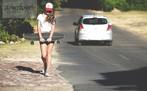 Junge Frau  die mit einem Skateboard neben einer Straße läuft.