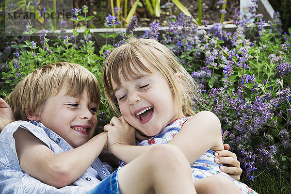 Ein lächelnder Junge und ein lächelndes Mädchen raufen sich  spielen zusammen im Freien in einem Garten.