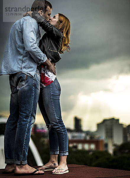Ein Paar  das auf einem Dach der Stadt steht und sich küsst.
