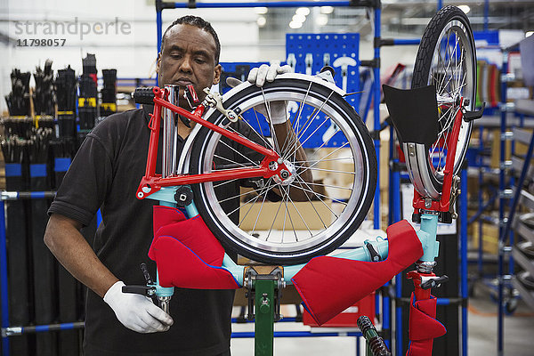 Männlicher Fabrikfacharbeiter  der in einer Fabrik ein Fahrrad zusammenbaut und ein Rad anbringt.