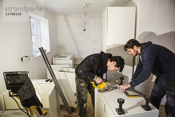 Zwei Bauarbeiter  die mit einer Kreissäge Gipskartonplatten für eine Küchenzeile zuschneiden.