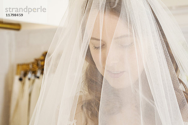 Kopf und Schultern einer Frau  die in einem auf Brautkleider spezialisierten Geschäft einen Brautschleier mit Netz anprobiert.