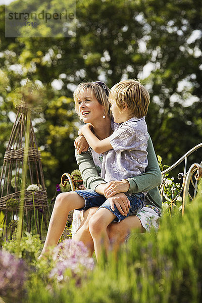 Frau sitzt in einem Garten mit einem Jungen auf dem Schoß und umarmt sich.