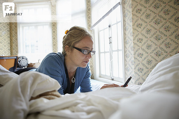 Frau benutzt Mobiltelefon auf dem Bett