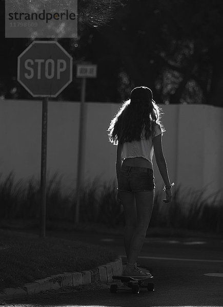 Rückansicht einer jungen Frau auf einem Skateboard an einer Straßenkreuzung.