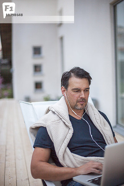 Mann benutzt Laptop auf der Veranda