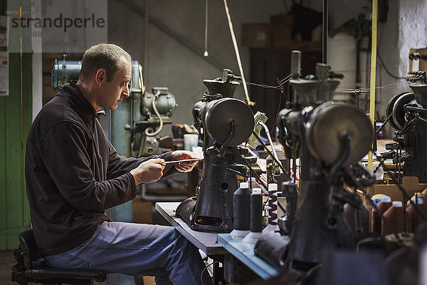 Mann sitzt an einer Nähmaschine in einer Schusterwerkstatt.