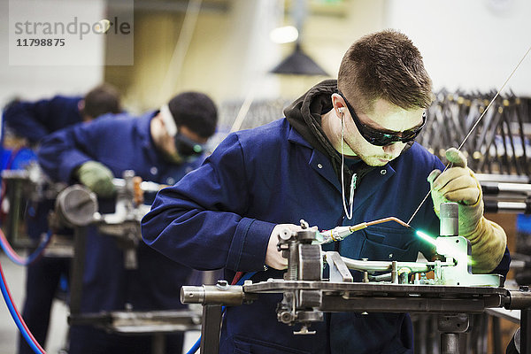 Männlicher Fabrikfacharbeiter mit Schutzbrille  der in einer Fabrik einen Teil eines Fahrrads zusammenschweißt.