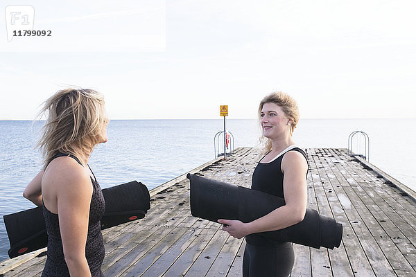 Zwei Frauen halten Turnmatten und unterhalten sich am Pier
