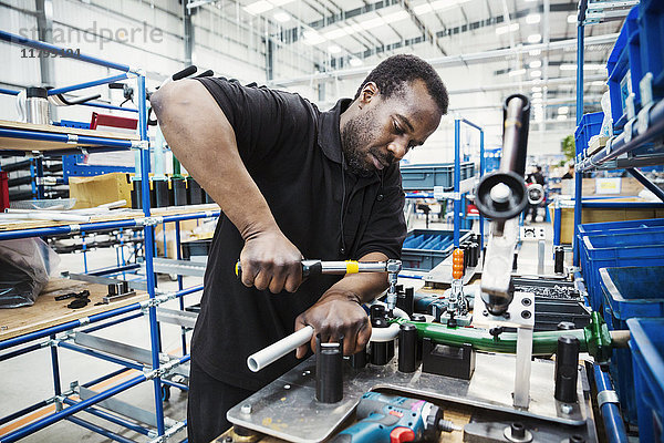 Männlicher Fabrikfacharbeiter  ein Mann mit einem Werkzeug in der Hand  der in einer Fabrik Teile eines Fahrrads zusammenbaut.