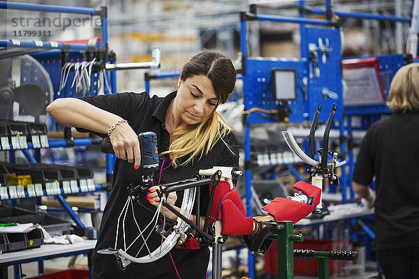 Fabrikfacharbeiterin  die in einer Fabrik ein Fahrrad zusammenbaut und an Rahmen und Rädern arbeitet.
