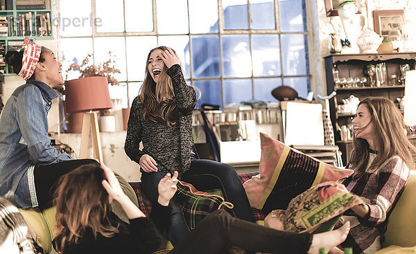Vier junge Frauen sitzen drinnen auf einem Sofa und lachen.