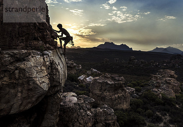 Bergsteiger  der eine Felsformation in einer gebirgigen Landschaft besteigt.