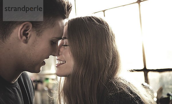 Ein lächelnder junger Mann und eine lächelnde junge Frau lehnen sich für einen Kuss an.