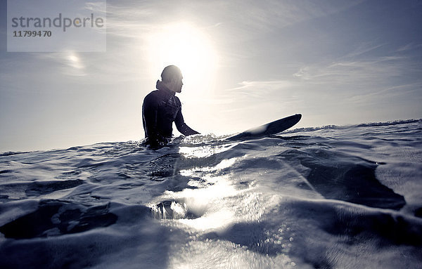 Surfer im Neoprenanzug auf einem Surfbrett im Meer sitzend.