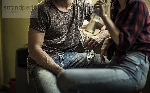 Ein Mann und eine Frau sitzen und trinken aus Glasflaschen auf Hockern an einer Bar.