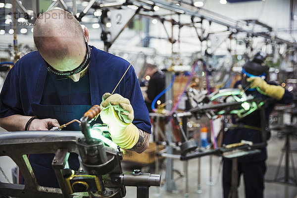Männlicher Fabrikfacharbeiter  der in einer Fabrik Schweißwerkzeuge an einem Fahrradrahmen benutzt.