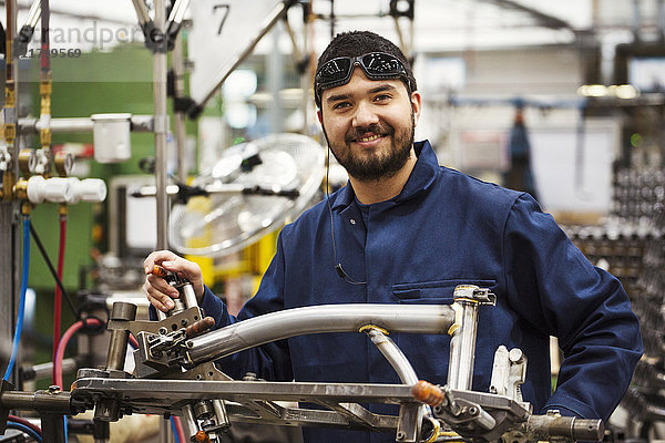 Männlicher Fabrikfacharbeiter mit einem teilweise montierten Fahrradrahmen in einer Fabrik.