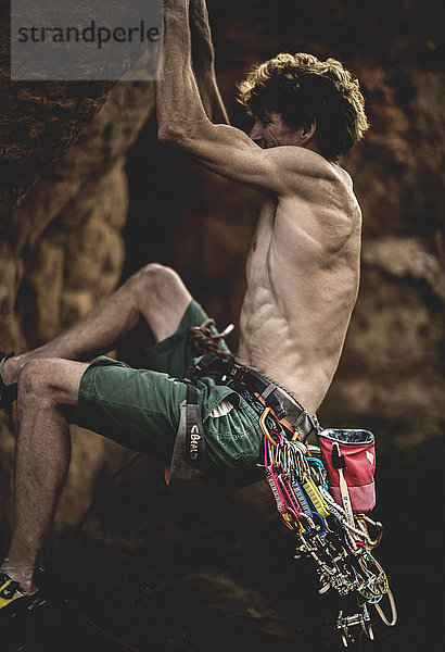 Bergsteiger mit nackter Brust  der mit Karabinerhaken und Seil eine Felsformation erklimmt.
