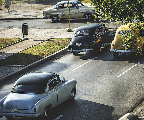 Klassische Autos aus den 1950er Jahren  die auf einer Straße an einer Kreuzung fahren.
