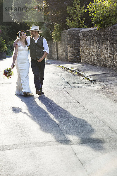 Braut und Bräutigam gehen eine ländliche Straße entlang.