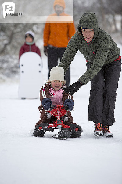 Mutter  die einem Mädchen beim Schlittenfahren im Schnee hilft