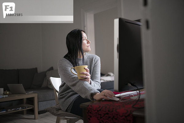 Frau hält Tasse  sitzt am Computer