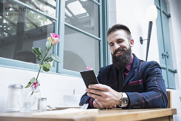 Junger Mann lächelt bei der Benutzung eines Mobiltelefons in einem Café