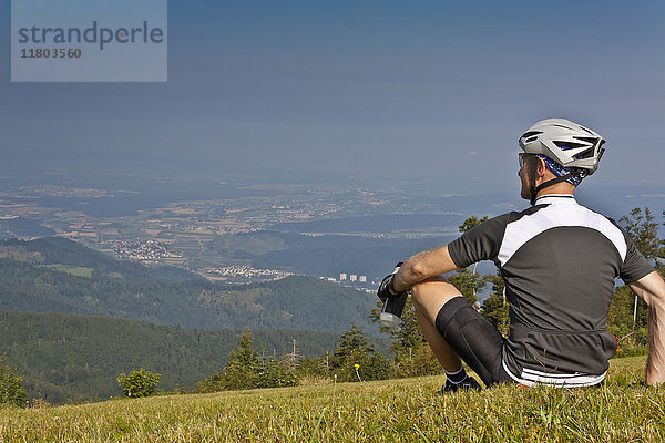 Mountainbiker  der sich auf einer Wiese ausruht und die Aussicht im Schwarzwald genießt
