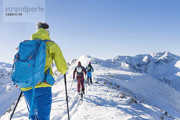 Rückansicht von Skifahrern  die auf einem Bergkamm gegen den Himmel laufen