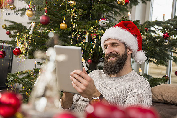 Junger Mann mit digitalem Tablet und Weihnachtsmannmütze