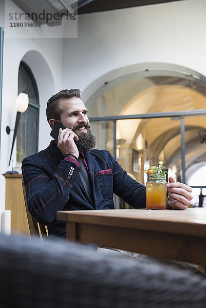 Junger Mann telefoniert mit einem Glas Saft in der Hand