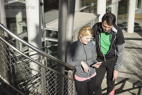 Mann und Frau in Sportkleidung benutzen Smartphone mit Kopfhörern