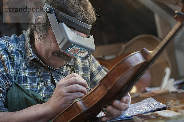 Geigenbauer malt Geige mit Vergrößerung