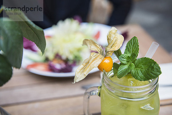 Blick auf gelben Mocktail im Glas neben einer Schüssel mit Salat