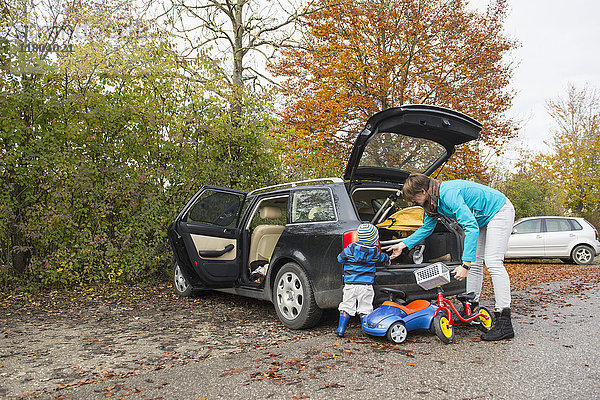 Mutter und Sohn packen ein Laufrad aus dem Kofferraum eines Autos in einer Herbstlandschaft