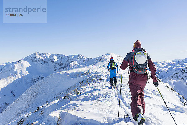 Rückansicht von Skifahrern  die auf einem Bergkamm gegen den Himmel laufen