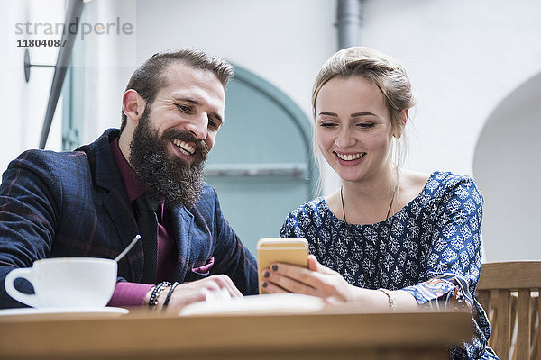 Junges Paar lächelt in einem Café und benutzt ein Mobiltelefon