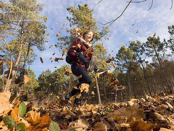 Teenager-Mädchen trägt ihre Schwester huckepack und läuft im Wald