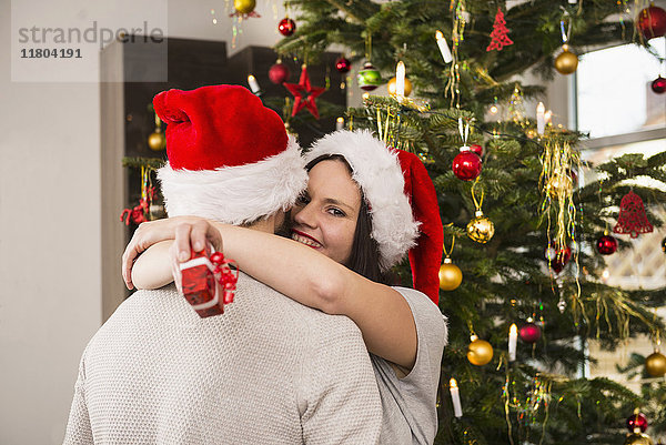 Frau mit Weihnachtsgeschenk  die ihren Mann umarmt