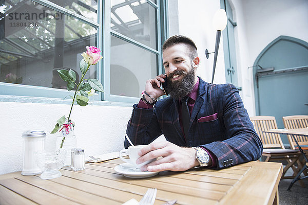 Junger Mann spricht mit dem Handy und hält eine Kaffeetasse in einem Café