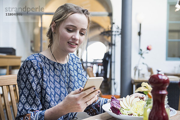 Junge Frau  die ein Mobiltelefon benutzt  während sie im Restaurant sitzt