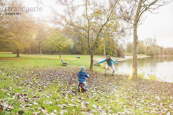 Kleiner Junge fährt mit seinem Laufrad in Richtung seiner Mutter in einer Herbstlandschaft