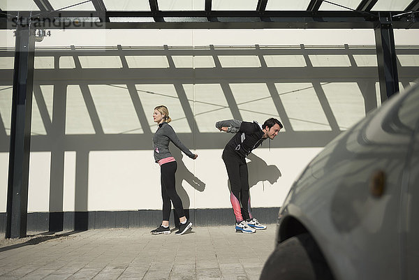 Mann und Frau in Sportkleidung beim Stretching auf dem Fußweg in der Stadt