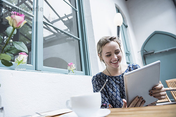 Lächelnde junge Frau mit digitalem Tablet in einem Café